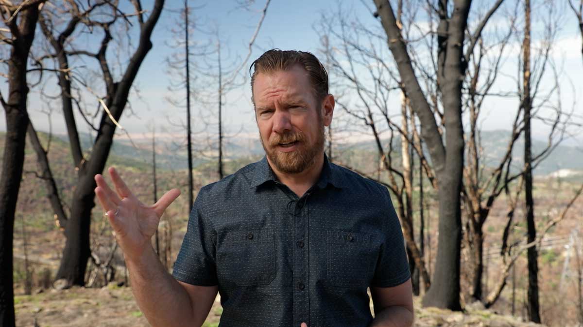 man talking in front of burned trees