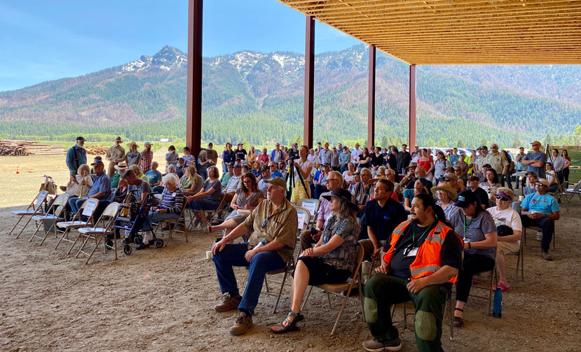 large group of people sit in chairs under and awning with mountains in the background