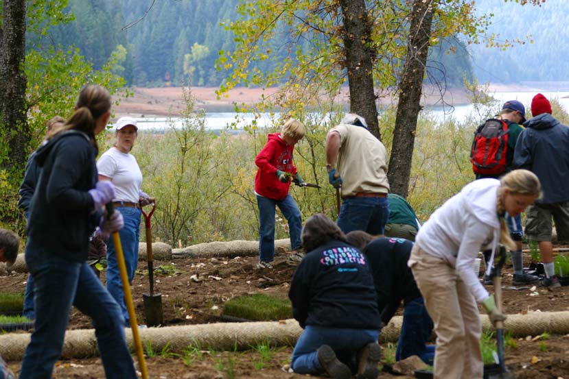 several people working with shovels with a lake and forest in the background