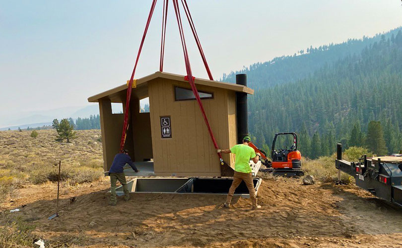 small restroom facility is being lowered to the ground as two people support it