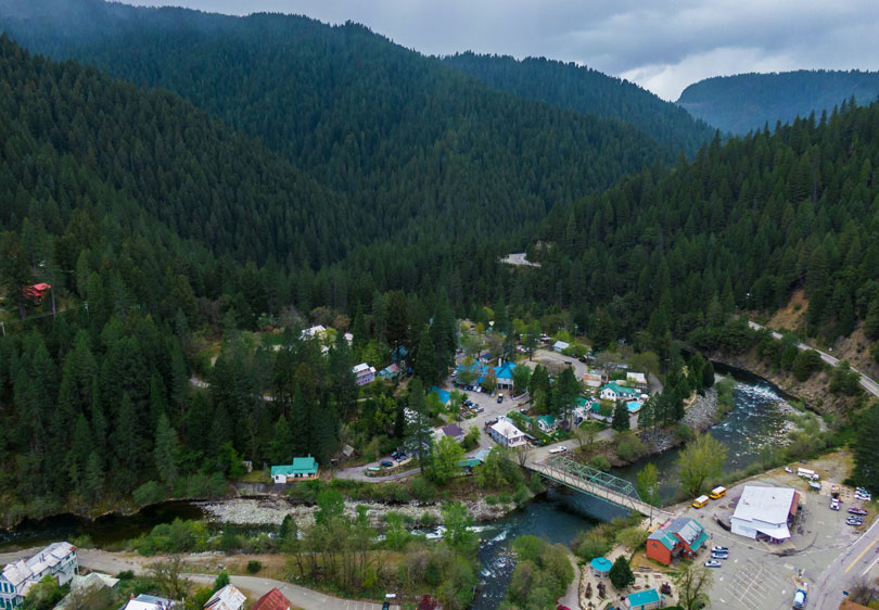 aerial looking down at a small town along a river surrounded by steep mountains blanketed in green trees