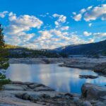 Calm alpine lake surrounded by granite and conifer trees.