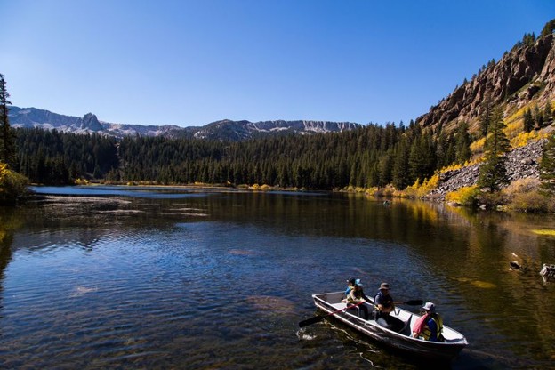 Three people in a paddleboat on a lake with trees and mountains in the background