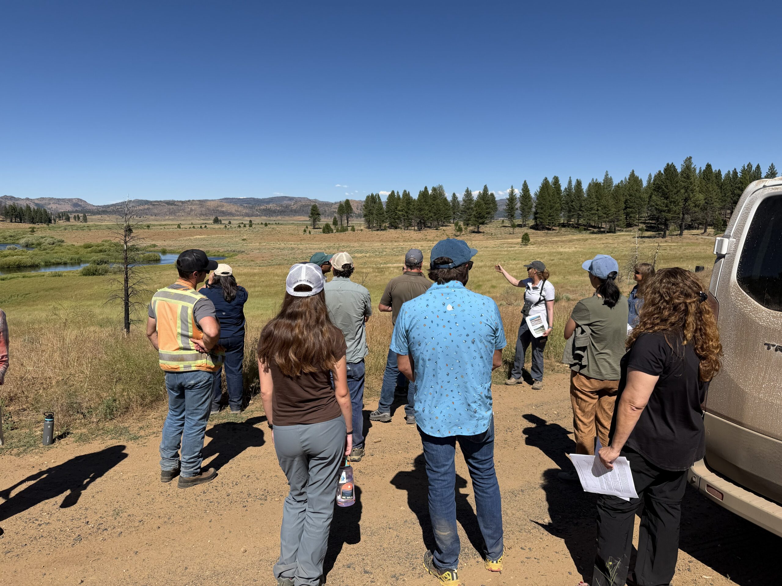 A tour group views an open landscape from a dirt road